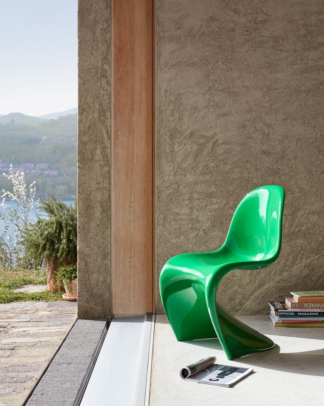 Verner Panton - Chaise S ou Panton verte, mise sur une terasse au bord de la mer bien &eacute;clair&eacute;e par le soleil. Par terre se trouve des magasines.